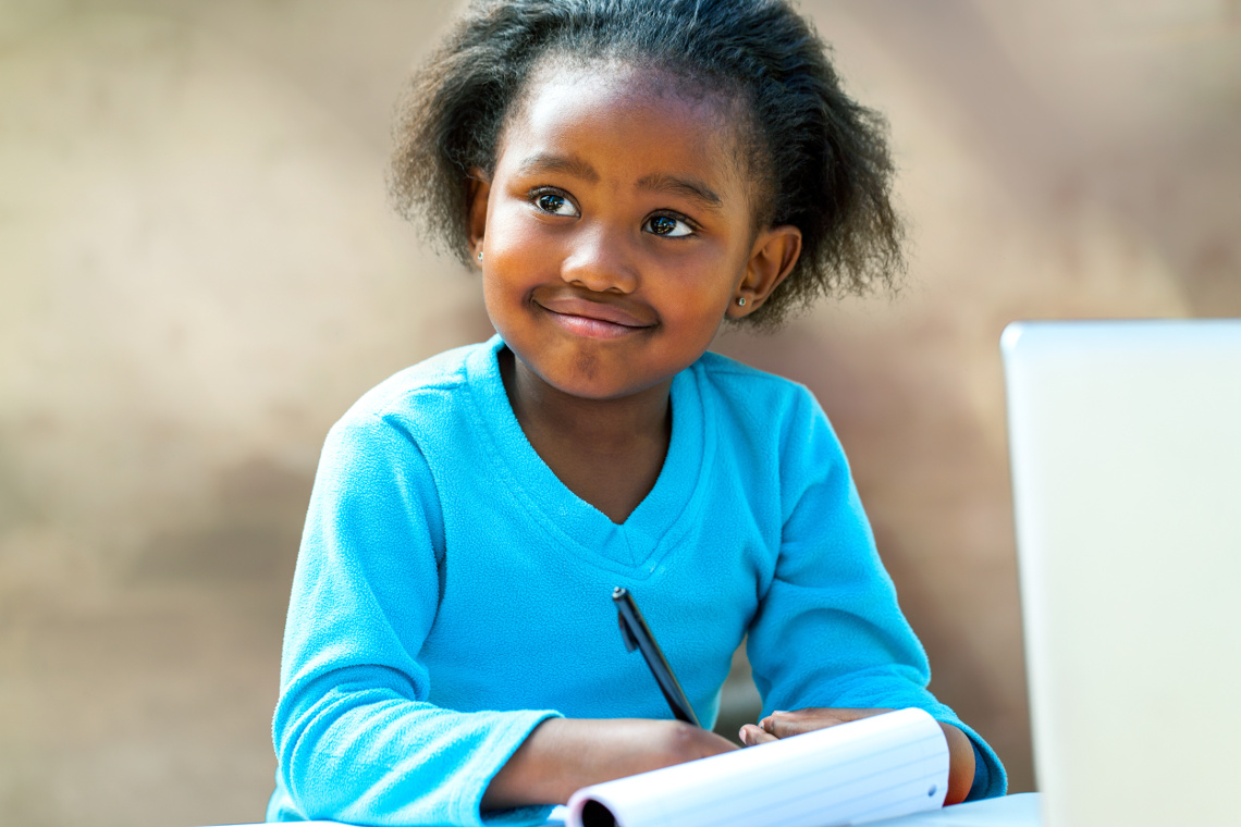 Portrait of african girl writing in notebook at desk.